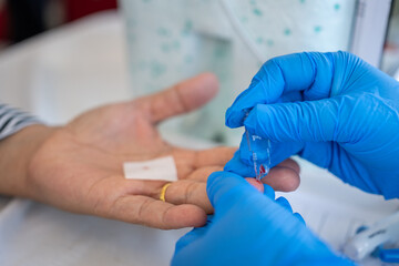 A healthcare worker wearing blue gloves collects a blood sample from a patient's fingertip using a...