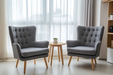 Two grey armchairs with wooden legs and a small round wooden table, placed in front of a window in a modern, minimalist living room.