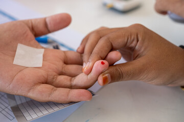 A healthcare worker performs a blood sugar test by pricking a patient's fingertip. A drop of blood...