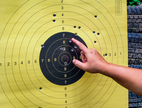 Close up photo of a man hands pointing at paper shooting target with numbers and bullet holes on it.
