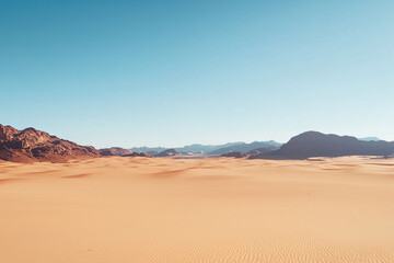 Fototapeta premium A vast desert landscape with towering mountain ranges in the distance, under a clear blue sky, showcasing nature’s raw beauty.