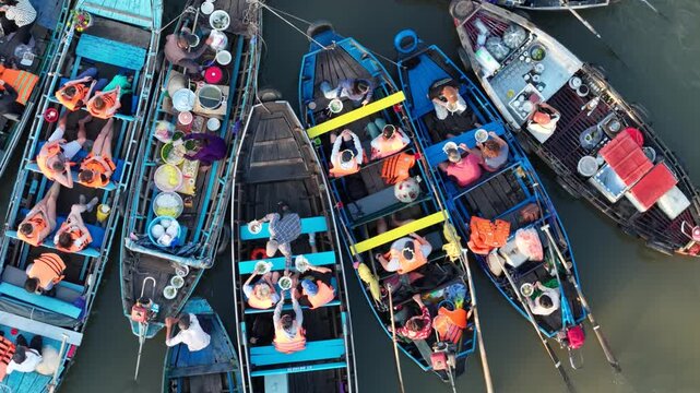 Drone view of tourists wearing life jackets enjoying local cuisine on boats at the bustling Cai Rang Floating Market, Can Tho, Vietnam.