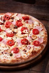 Pizza with ham, cherry tomatoes and mozzarella cheese. Wooden background. Soft focus. Close up.	