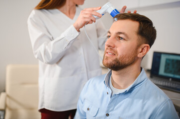 Female doctor looks at a man's scalp with a dermatoscope. Diagnosis of scalp condition by a...