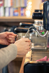 Barista steaming milk with coffee machine. Female barista making coffee in cafe.