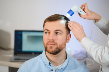 Female doctor looks at a man's scalp with a dermatoscope. Diagnosis of scalp condition by a...