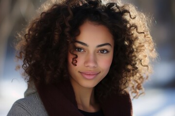 Fototapeta premium A young woman with beautiful curly hair radiates warmth and joy in a serene winter landscape, where soft light filters through the trees, enhancing her natural beauty and smile