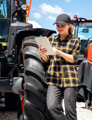 Woman using digital tablet while standing next to agricultural or construction machinery outdoors.