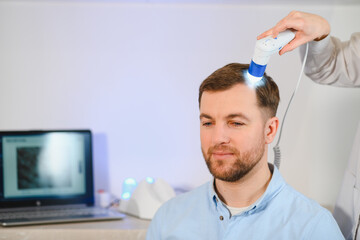 Female doctor looks at a man's scalp with a dermatoscope. Diagnosis of scalp condition by a...