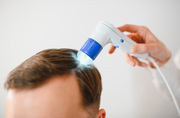 Female doctor looks at a man's scalp with a dermatoscope. Diagnosis of scalp condition by a trichologist. Mole examination, baldness, hair transplantation