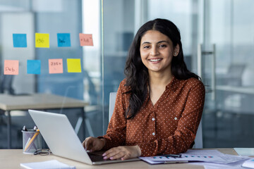 Successful businesswoman at workplace inside office working with laptop. Woman smiling and looking...