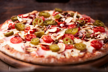 Pizza with ham, cherry tomatoes, jalapeno pepper and mozzarella cheese. Wooden background. Soft focus. Close up.
