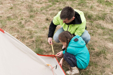 Family bonding under the open sky while setting up a colorful tent during a sunny day in the gentle...