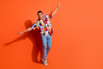 Vibrant young man poses confidently in front of an orange background, wearing a trendy colorful...