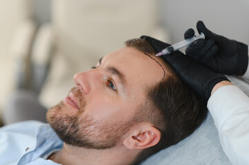 Fototapeta premium Side view of handsome man getting hair treatment at beauty salon. Man having mesotherapy session at aesthetic clinic, therapist hands in gloves making injection in scalp