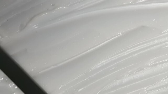 spatula glides through a thick, white mixture, blending it smoothly. macro video eye, face or body moisturizing cream