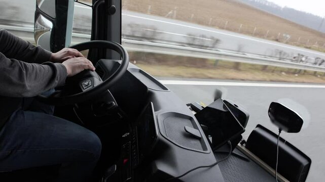Footage view of part of the driver's body in the cab of a moving truck. All potential trademarks are  blurred.