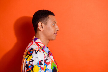 Stylish young man in vibrant colorful shirt stands against bright orange background, showcasing a...