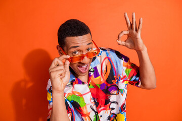 Charming man with vibrant fashion sense showcases confident pose against bright orange backdrop,...