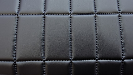 The surface texture of artificial leather in black, stitched in the form of diamonds, squares, rectangles. Quilted eco-leather. 