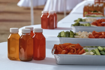 Vegetables and drinks on the table outdoors. Preparation for a large corporate lunch. Waiters in...