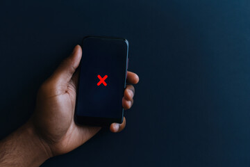 Hand holding smartphone showing red cross symbol on dark background