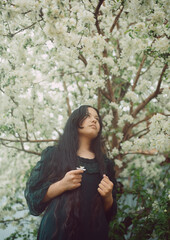 A dark-haired girl stands by a tree blooming in spring