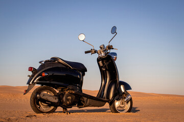 The Retro black scooter at sunset in the golden sand of the Namib Desert