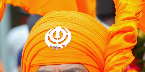 Sikh man wearing orange dastar with Khanda symbol during religious celebration