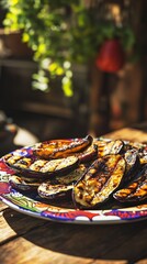 Grilled vegetables including eggplant, zucchini, and sweet peppers served on a bright plate with ethnic print, with rustic kitchen environment and green leaves in the background