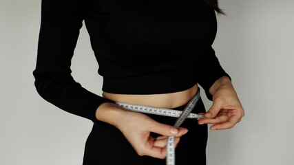 The girl tracks her progress in the process of weight loss, measures the volume and proportions of the body, while remaining active, while measuring the volume of her waist with a centimeter tape.