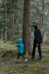 Fototapeta premium Exploring lush green woods hand in hand, a child and an older companion wander among ancient trees during a peaceful autumn afternoon adventure