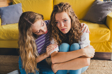 Young woman comforting her friend as they sit together on living room floor, highlighting supportive friendship and emotional bonding