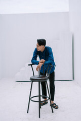 Contemplative young man leaning against a chair in minimalist white space