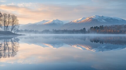 Fototapeta premium Misty sunrise over snow-capped mountains reflecting in calm lake