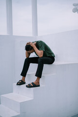 Contemplative man seated on steps with hands clasped on his head in distress