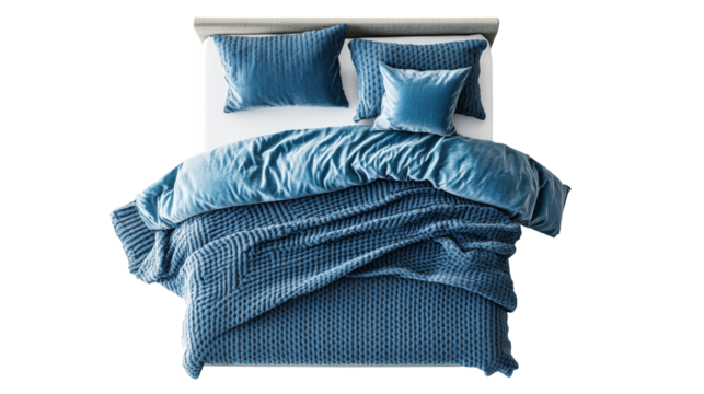 A beautifully arranged blue blanket draped over a bed, complemented by plush pillows, showcasing detailed textures and soft shadows under natural light.