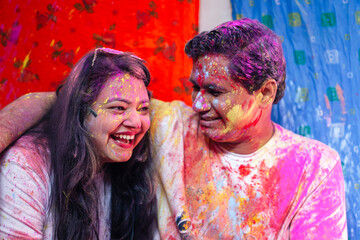 A playful and happy Indian couple is playing with vibrant Holi colors during the Indian festival of colors, Holi, which symbolizes love and tradition.