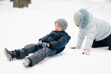Children having fun sliding on snow in winter park