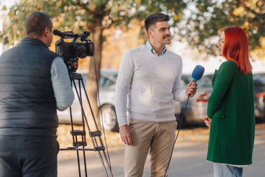 Journalist interviewing businesswoman for television news story outdoors