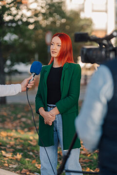 Journalist interviewing young woman with red hair in a park
