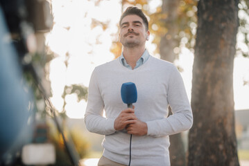 Male journalist reporting live news with microphone in park