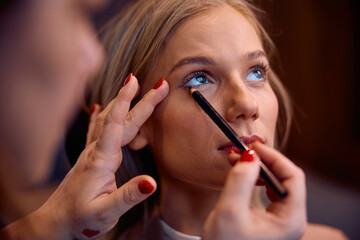 Close up of make up artist applying eyeliner during young woman's treatment at professional salon.