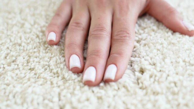 a woman's hand touching the beige Interior pile carpet made of polypropylene. 