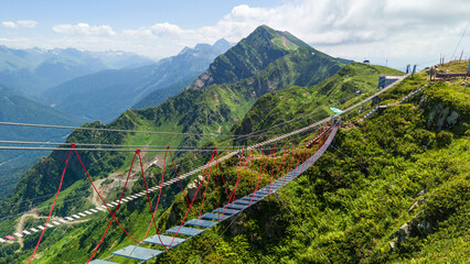 Suspension bridge over lush mountain range at Rosa Khutor resort near Sochi, Russia, with scenic...