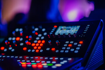 A close-up of a professional audio mixing console with illuminated buttons and knobs in a dimly lit...