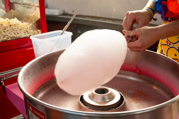 A person is making cotton candy. The cotton candy is being made in a machine. The machine is silver and red