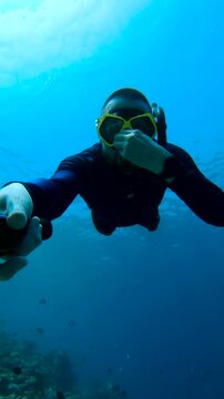 A freediver explores underwater in the Maldives, using a camera while wearing a mask and snorkel. Location: underwater, Maldives.
