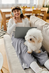 Young woman enjoys cozy afternoon at home with her fluffy dog and laptop