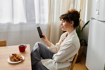 Young woman savors coffee and croissants while leisurely checking her phone
